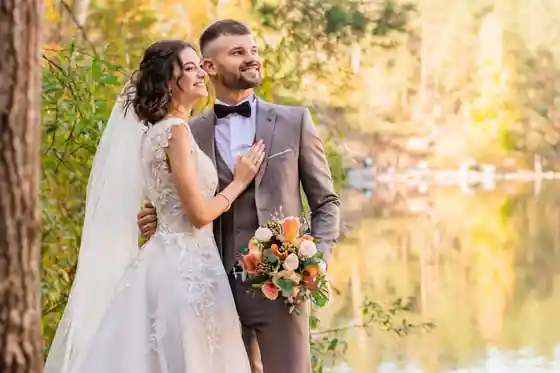 Couple full-body photo by lake, structured satin bridal dress